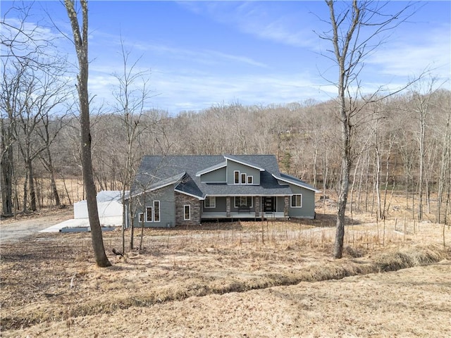 view of front facade featuring a forest view, a shingled roof, and a porch