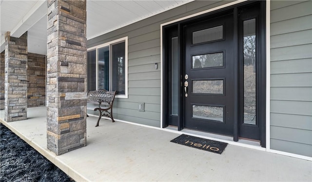 view of exterior entry featuring stone siding and covered porch