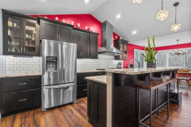 kitchen with stainless steel appliances, dark wood-type flooring, vaulted ceiling, wall chimney range hood, and a kitchen bar