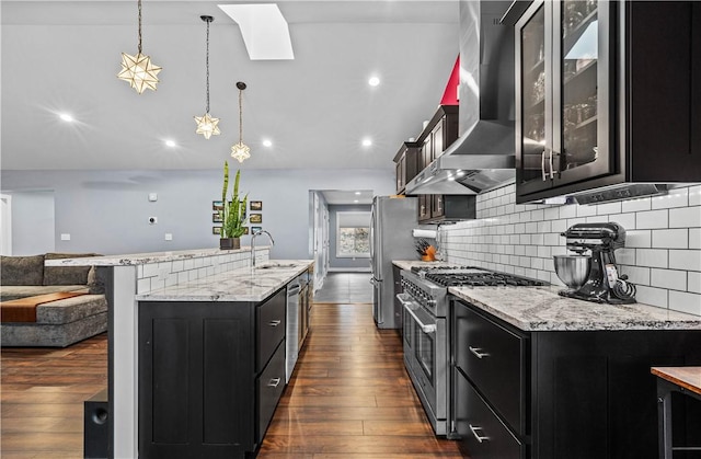 kitchen with wall chimney exhaust hood, dark wood-type flooring, dark cabinets, stainless steel appliances, and a sink