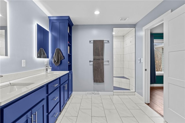 bathroom featuring a tile shower, double vanity, a sink, and visible vents