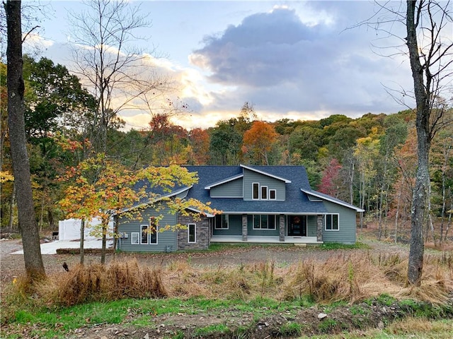 view of front facade featuring a shingled roof and a forest view