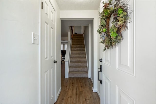 hall with baseboards, stairway, a textured ceiling, and wood finished floors