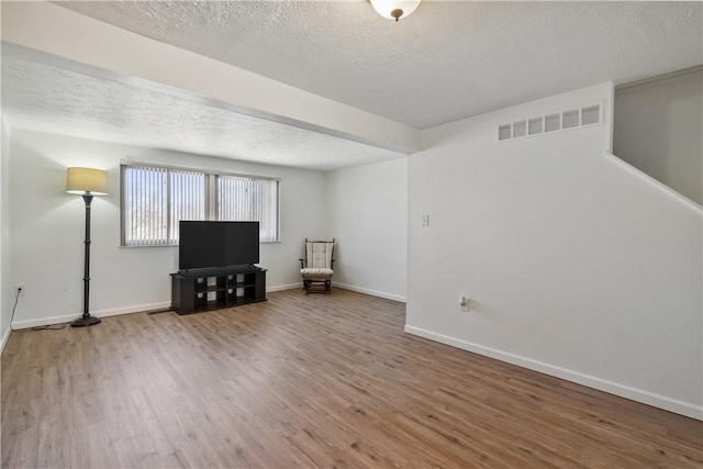 unfurnished living room featuring a textured ceiling, wood finished floors, visible vents, and baseboards