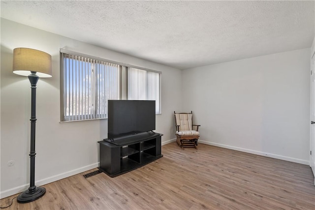 living area with a textured ceiling, baseboards, and wood finished floors