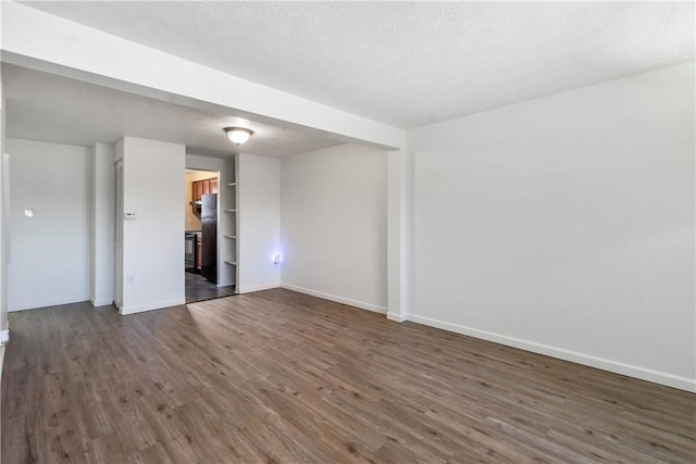 spare room featuring a textured ceiling, dark wood-type flooring, and baseboards