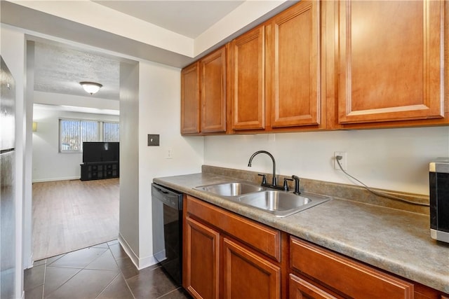 kitchen with black dishwasher, brown cabinetry, a sink, dark tile patterned flooring, and baseboards