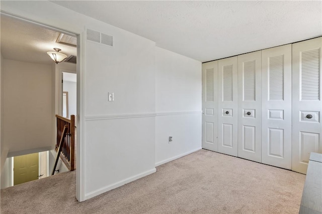 unfurnished bedroom with a textured ceiling, carpet floors, visible vents, baseboards, and a closet