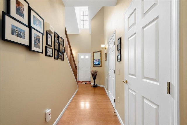 hall with light wood finished floors, stairway, a towering ceiling, and baseboards