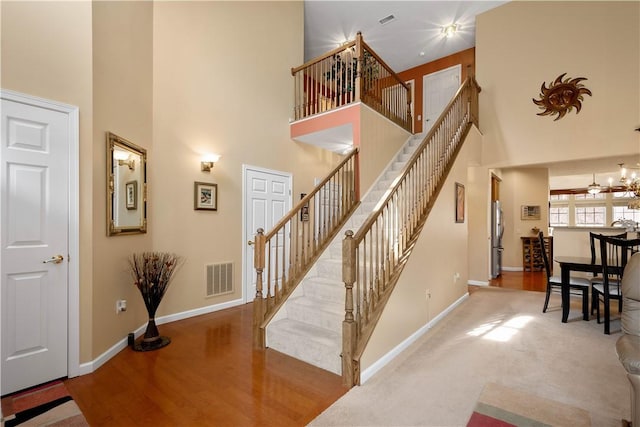 stairway featuring a high ceiling, wood finished floors, visible vents, and baseboards