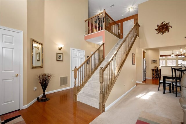 staircase featuring wood finished floors, an inviting chandelier, a towering ceiling, baseboards, and visible vents