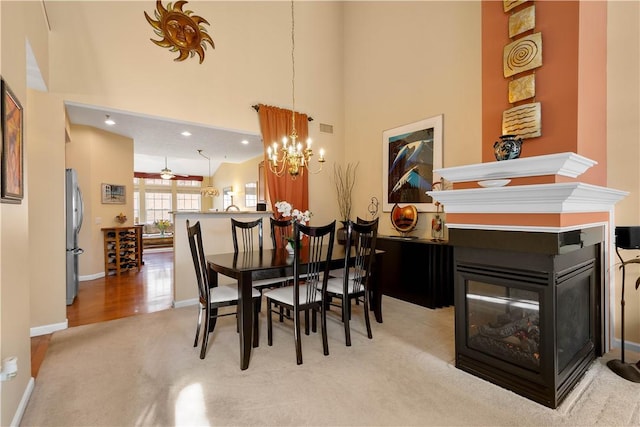 dining area with a towering ceiling, baseboards, visible vents, light colored carpet, and a multi sided fireplace