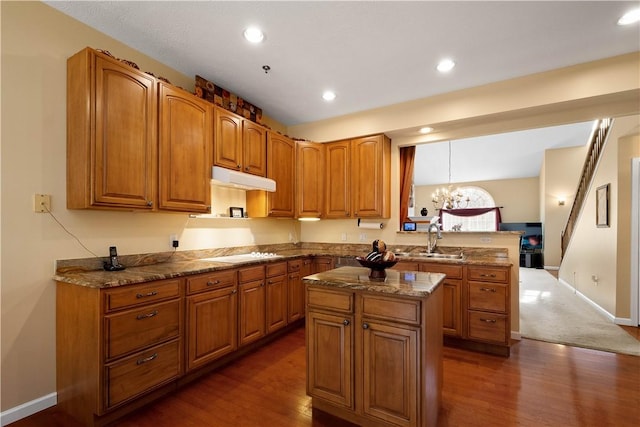 kitchen with stone counters, under cabinet range hood, a peninsula, a sink, and white cooktop