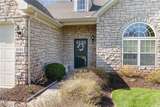 doorway to property featuring roof with shingles, stone siding, and a garage