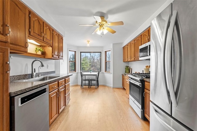 kitchen featuring appliances with stainless steel finishes, dark countertops, brown cabinetry, and a sink