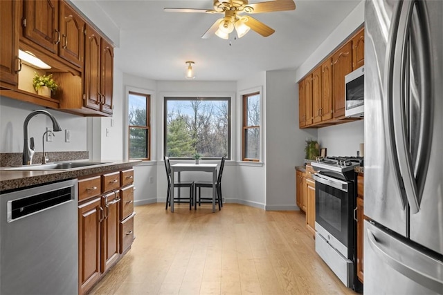 kitchen featuring brown cabinetry, a ceiling fan, appliances with stainless steel finishes, light wood-style floors, and a sink