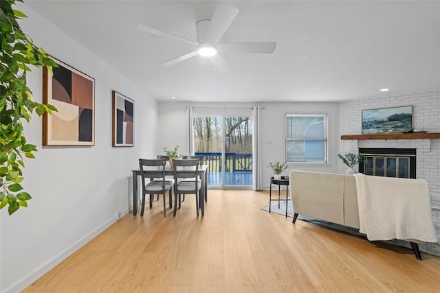 living room with a ceiling fan, a brick fireplace, baseboards, and wood finished floors