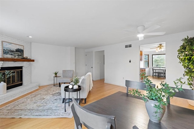 dining area featuring visible vents, light wood-style floors, a brick fireplace, ceiling fan, and baseboards