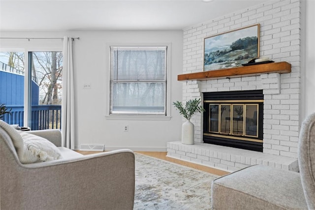 living area with a brick fireplace, visible vents, baseboards, and wood finished floors