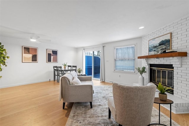 living area with a ceiling fan, a fireplace, baseboards, and wood finished floors