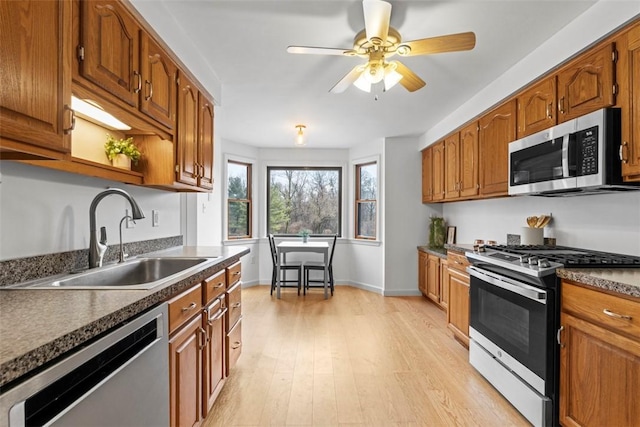 kitchen featuring appliances with stainless steel finishes, dark countertops, a sink, and light wood-style floors