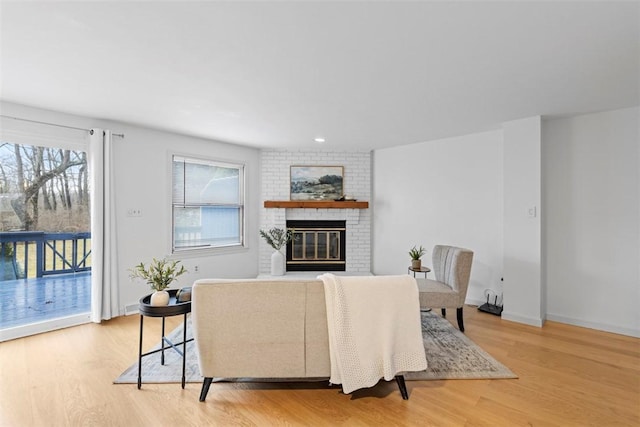 living area featuring light wood finished floors, a brick fireplace, and baseboards