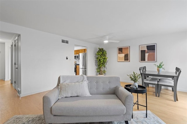 living area featuring light wood-style floors, visible vents, baseboards, and a ceiling fan