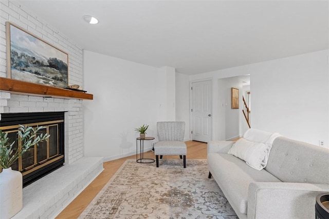 living room with a brick fireplace, baseboards, and wood finished floors