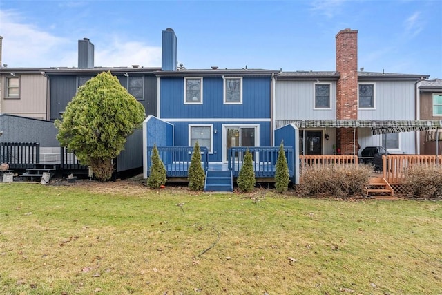 back of property with a lawn, a chimney, and a wooden deck