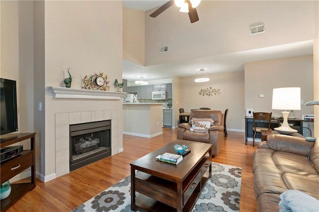 living area with a ceiling fan, visible vents, a tiled fireplace, and light wood finished floors