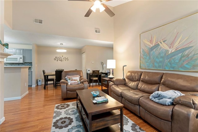 living area featuring light wood-style floors, a high ceiling, visible vents, and a ceiling fan