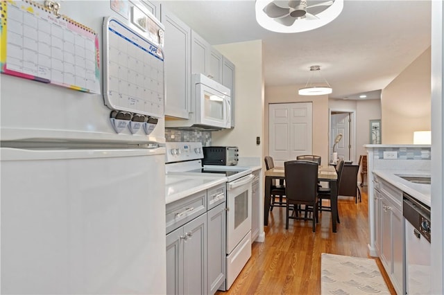 kitchen with tasteful backsplash, light countertops, light wood-style flooring, gray cabinetry, and white appliances