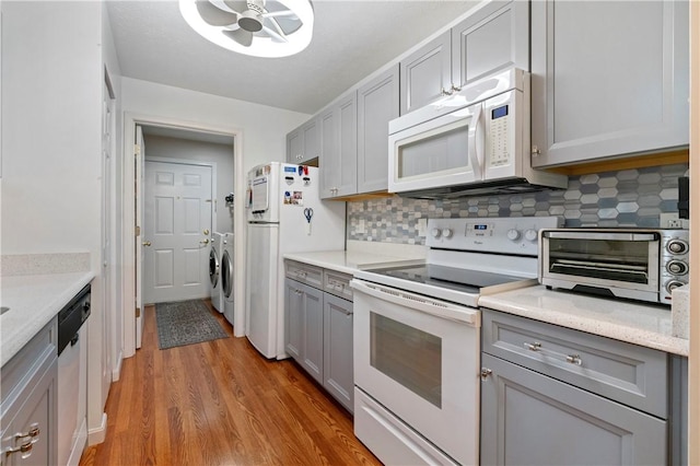 kitchen featuring white appliances, a toaster, decorative backsplash, washing machine and clothes dryer, and gray cabinets