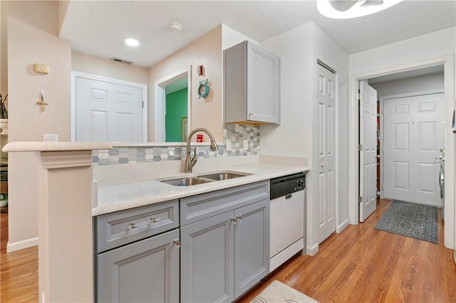 kitchen featuring visible vents, white dishwasher, gray cabinets, light countertops, and a sink