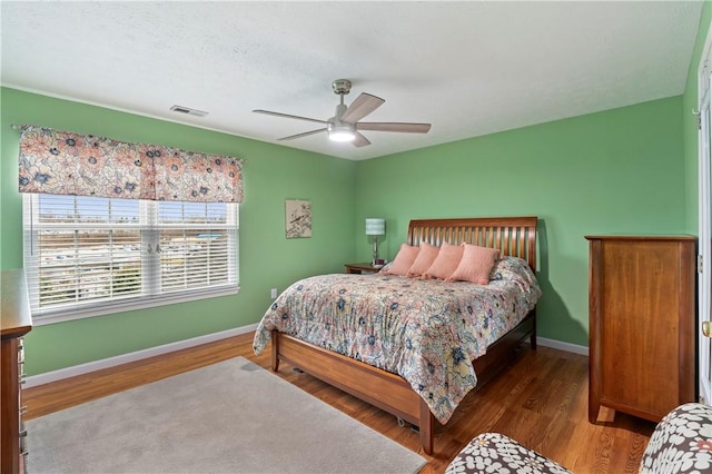 bedroom with baseboards, visible vents, ceiling fan, and wood finished floors