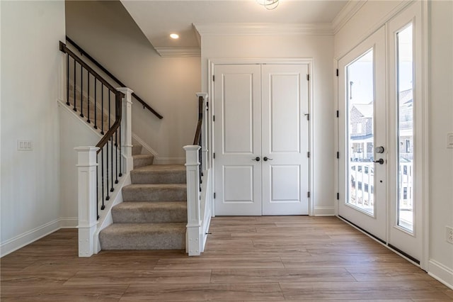 entryway featuring light wood-style flooring, stairs, ornamental molding, and baseboards