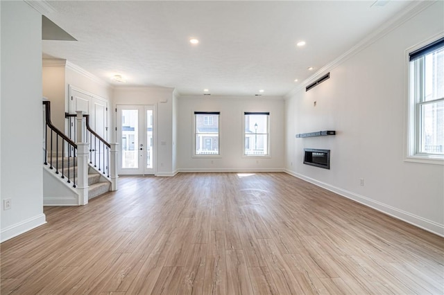 unfurnished living room with stairs, light wood-type flooring, a glass covered fireplace, and a wealth of natural light