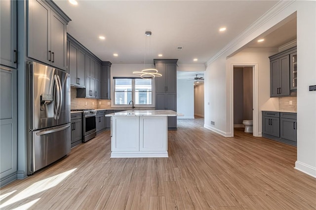 kitchen featuring light wood-style flooring, a kitchen island, baseboards, appliances with stainless steel finishes, and backsplash