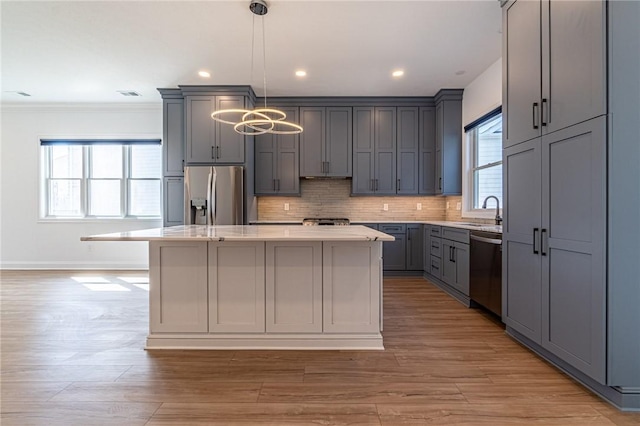 kitchen with gray cabinetry, a sink, appliances with stainless steel finishes, a center island, and tasteful backsplash