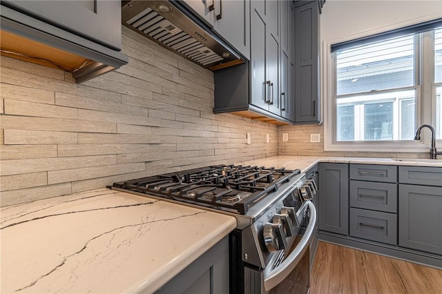 kitchen with light stone counters, gray cabinets, a sink, gas range, and under cabinet range hood