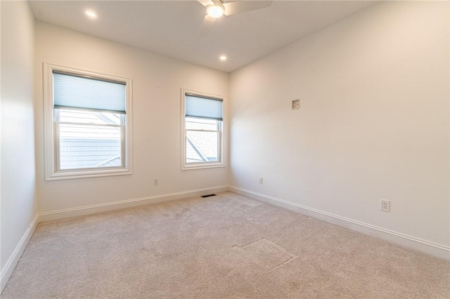 empty room featuring a ceiling fan, light colored carpet, visible vents, and baseboards