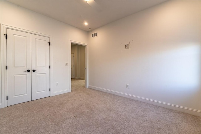 unfurnished bedroom featuring baseboards, visible vents, light colored carpet, ceiling fan, and a closet