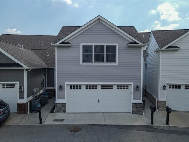 view of front of home with an attached garage, stone siding, and roof with shingles