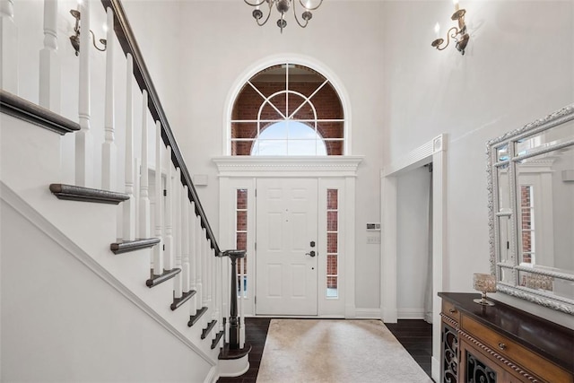 foyer with stairs, a high ceiling, dark wood-type flooring, and a notable chandelier