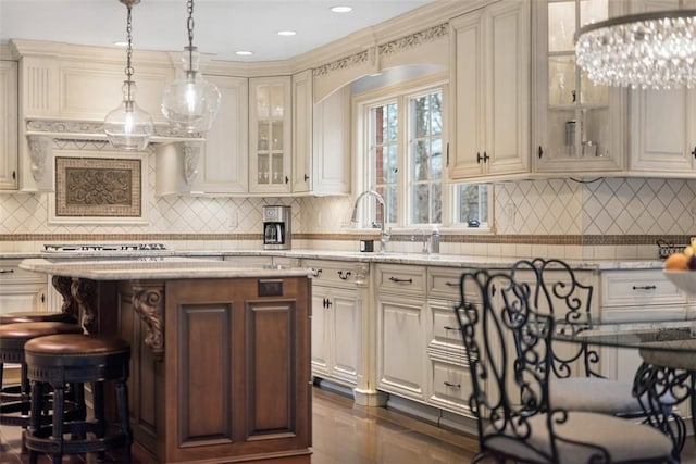 kitchen featuring hanging light fixtures, light stone countertops, a kitchen island, and cream cabinetry