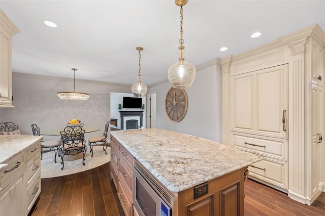 kitchen with light stone counters, a center island, dark wood finished floors, stainless steel microwave, and ornamental molding