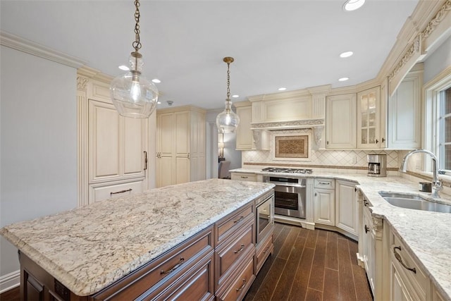 kitchen featuring cream cabinets, appliances with stainless steel finishes, dark wood-type flooring, a sink, and light stone countertops