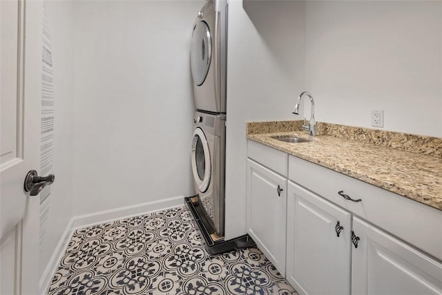 clothes washing area with stacked washer and dryer, dark tile patterned floors, a sink, baseboards, and cabinet space