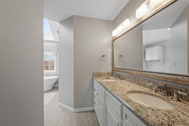 full bathroom with double vanity, a freestanding tub, a sink, and baseboards