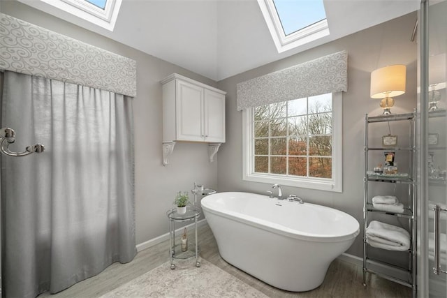 full bathroom featuring a freestanding tub, baseboards, lofted ceiling with skylight, and wood finished floors